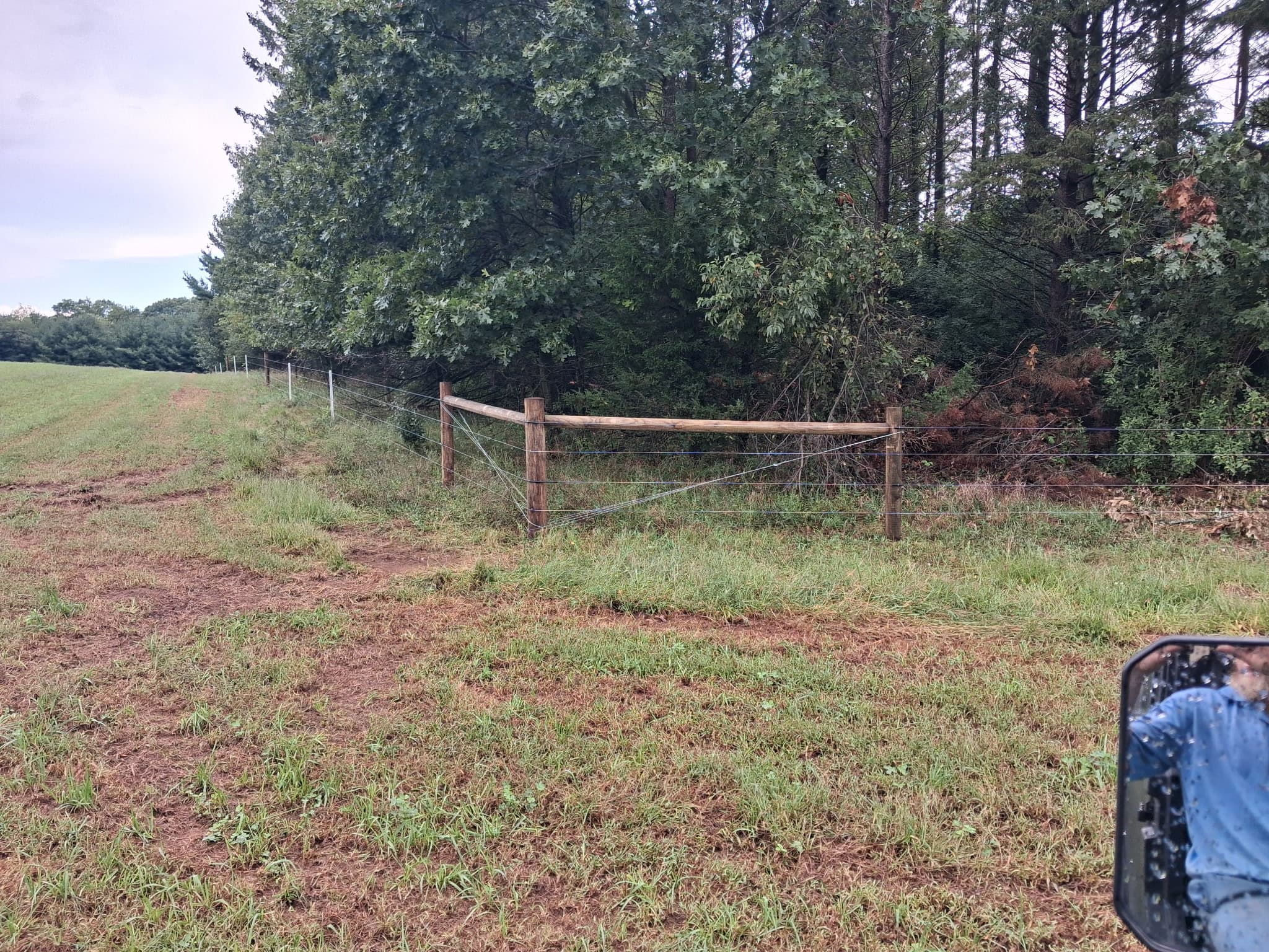 Wood-braced corner in a wire fence running beside a wooded pasture.
